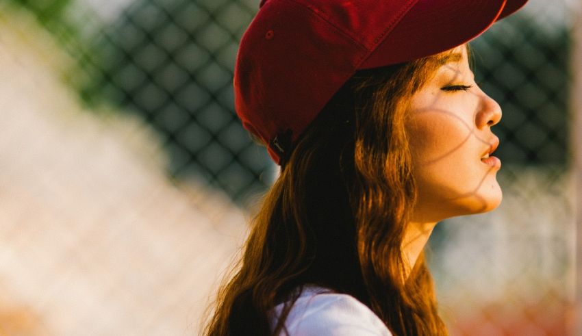 A woman wearing a red baseball cap in front of a fence.