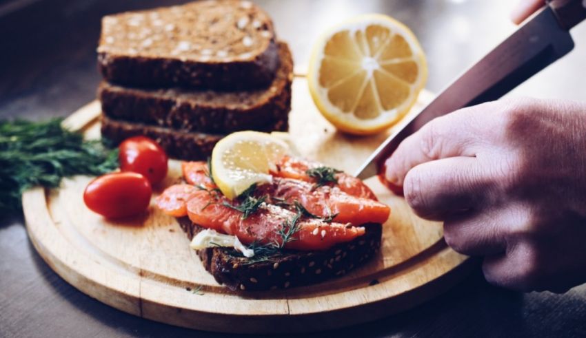 A person cutting a piece of salmon on a wooden cutting board.