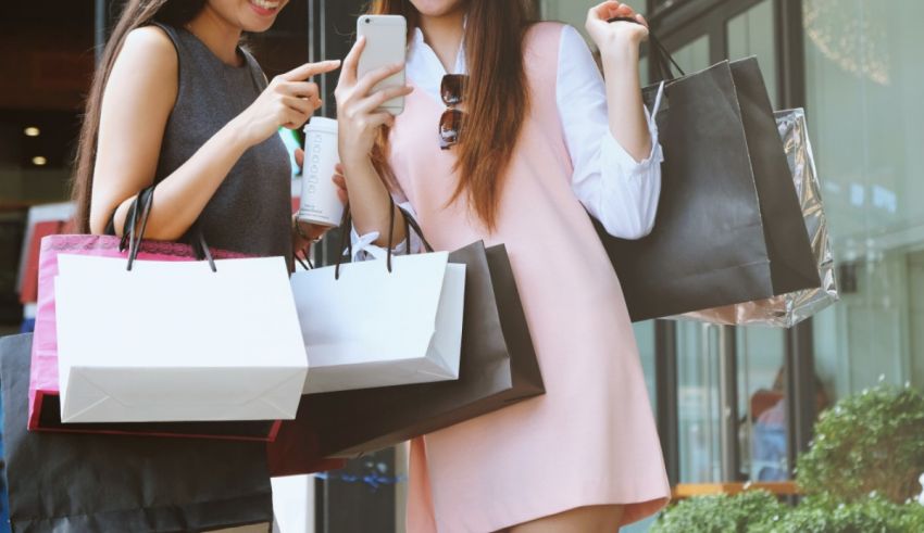 Two women holding shopping bags and looking at their phones.
