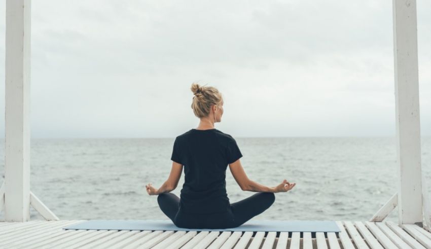 A woman meditating on a deck overlooking the ocean.
