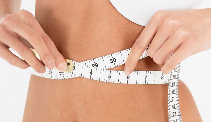 A woman measuring her waist with a measuring tape.