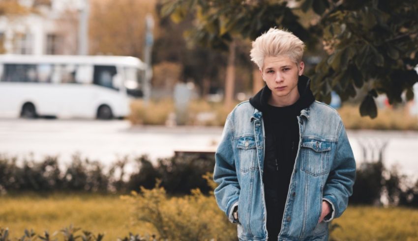 A young man in a denim jacket standing in front of a bus.