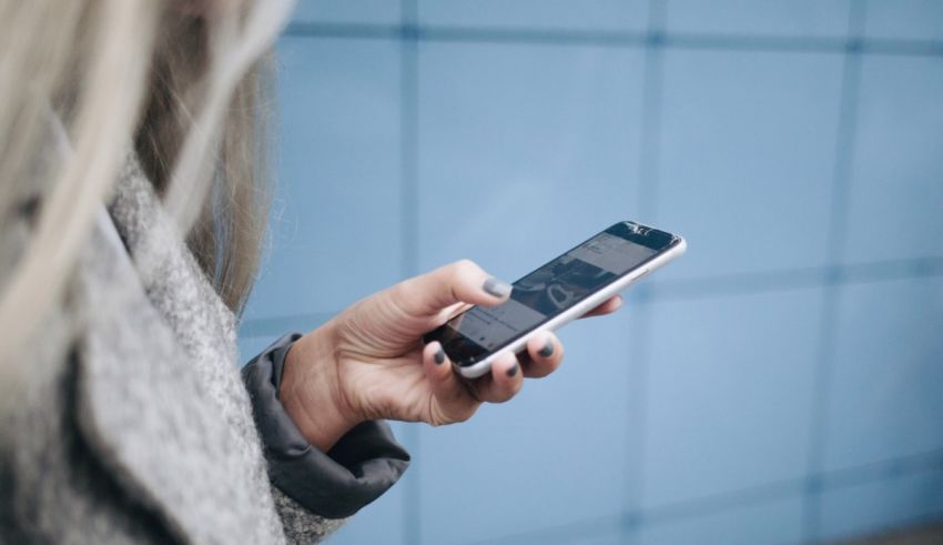 A woman holding a cell phone in front of a blue wall.