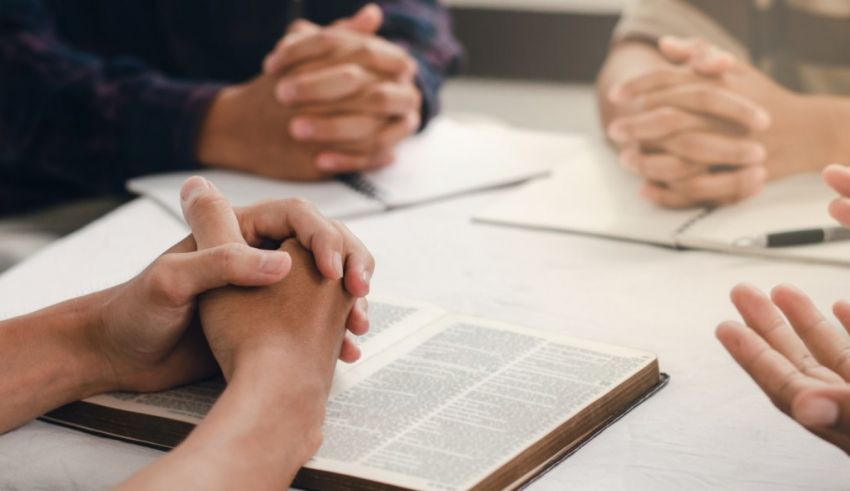 A group of people holding hands at a table with a bible.