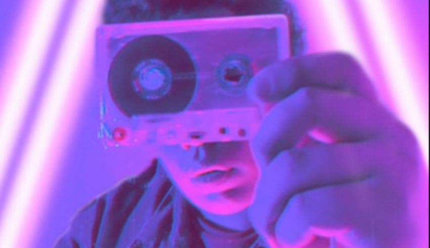 A man holding a cassette in front of a purple light.