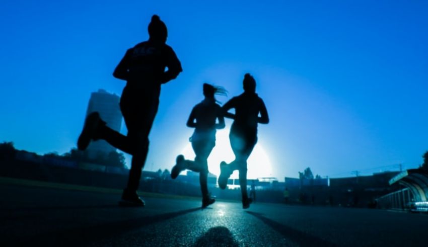 Silhouettes of people running on a road at dusk.