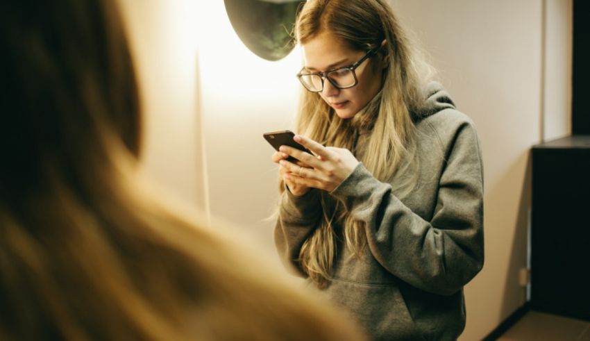 A woman is looking at her phone in front of a mirror.