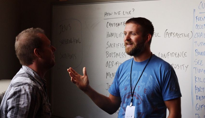 Two men in front of a whiteboard talking to each other.