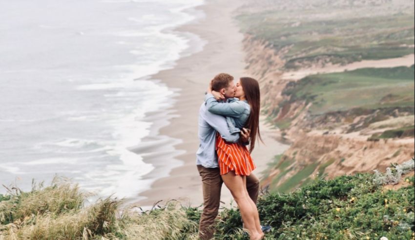 A couple kissing on a cliff overlooking the ocean.