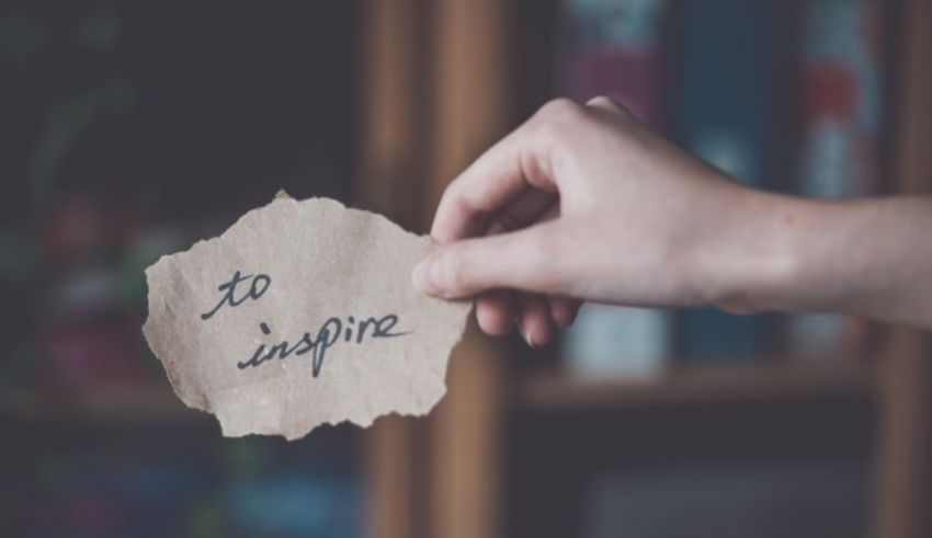 A hand holding a piece of paper with the word inspire written on it.