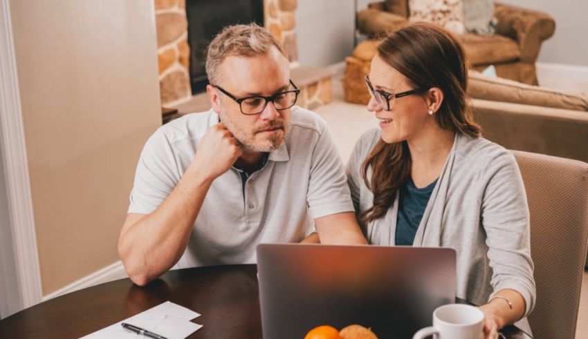 A man and woman sitting at a table looking at a laptop.