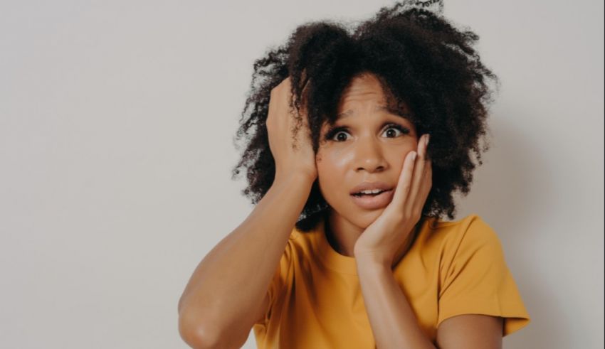 A woman with afro hair covering her face with her hands.