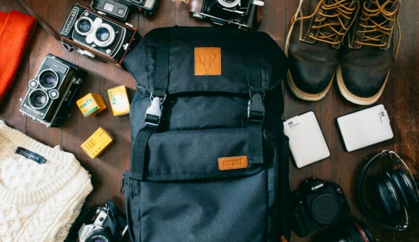 A backpack, camera and other items are laid out on a wooden table.