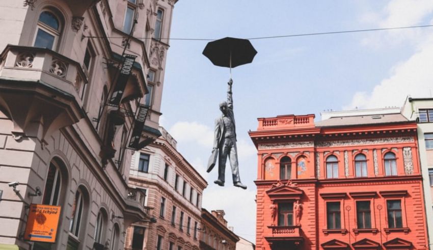 A man with an umbrella hanging from a wire in a city.
