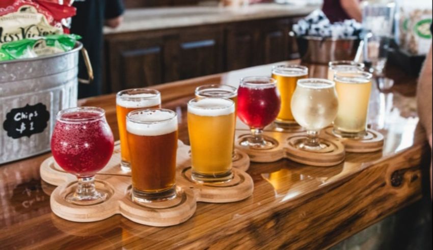 A line of different types of beer on a wooden bar.
