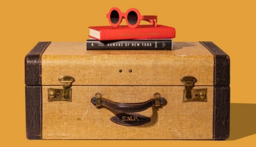A suitcase with a book and sunglasses on top.