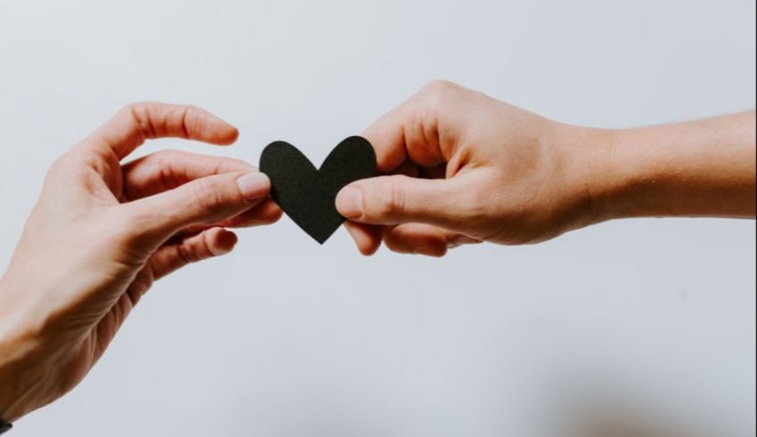Two hands holding a black heart shaped paper.