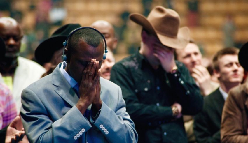 A man in a cowboy hat is praying in front of a crowd.