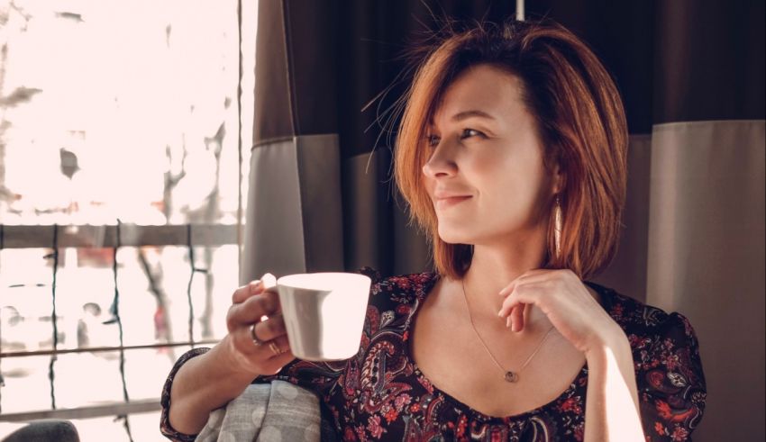 A woman holding a coffee mug in front of a window.