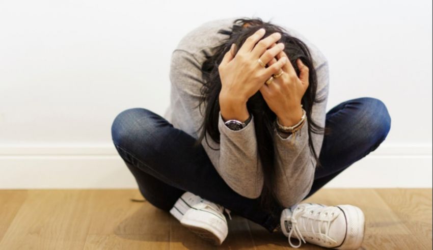 A woman sitting on the floor with her hands on her face.