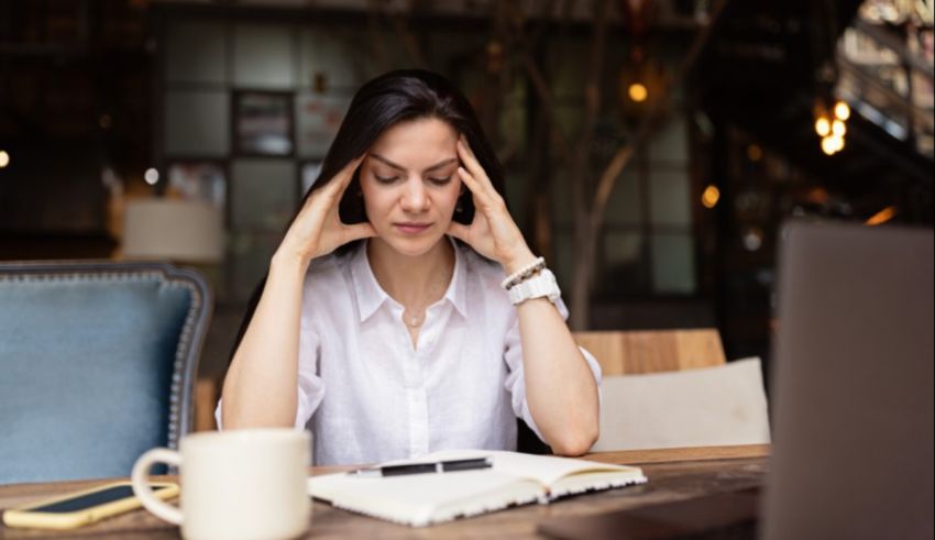 A woman is sitting at a table with her hands on her head.