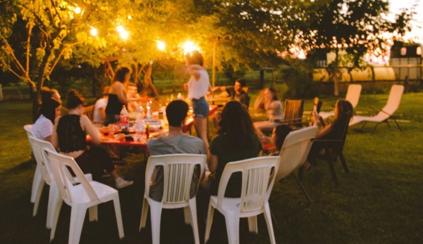 A group of people sitting around a table in a yard at dusk.