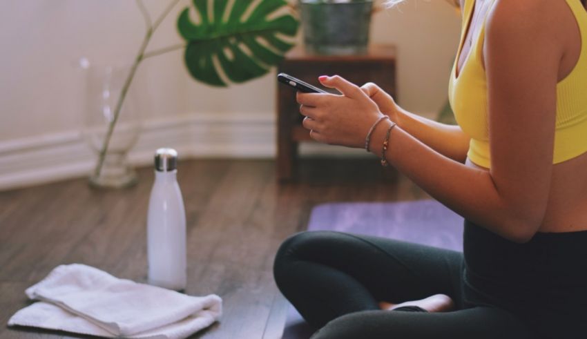A woman sitting on a yoga mat and using her phone.