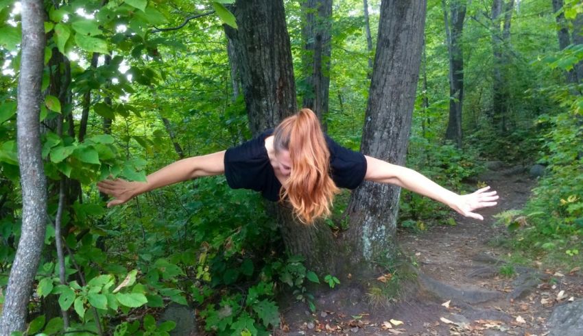 A woman in the woods with her arms outstretched.