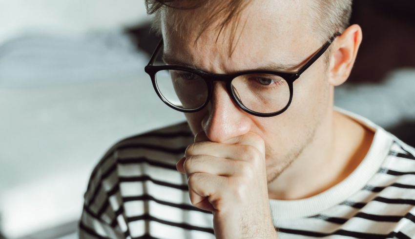 A man in glasses is sneezing with his hand on his chin.