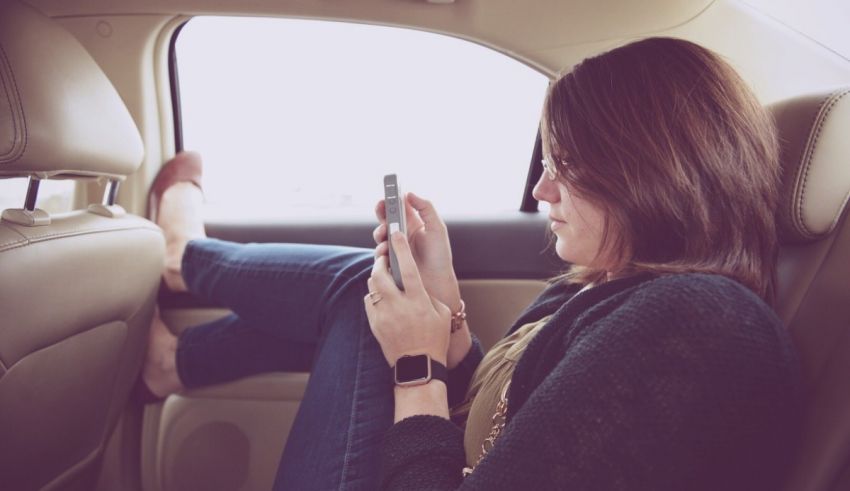 A woman sitting in the back seat of a car using her cell phone.