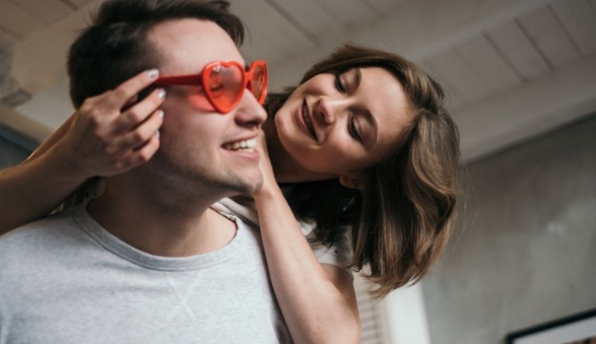 A man is holding a woman while wearing red heart shaped glasses.