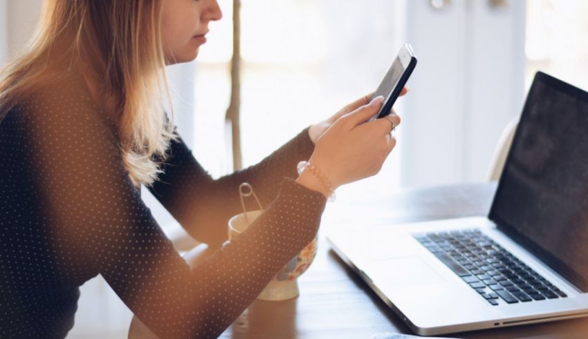 A woman sitting at a table with a laptop and cell phone.
