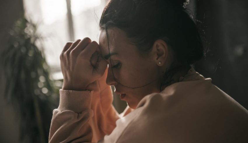 A woman is holding her head in her hands while sitting in front of a window.