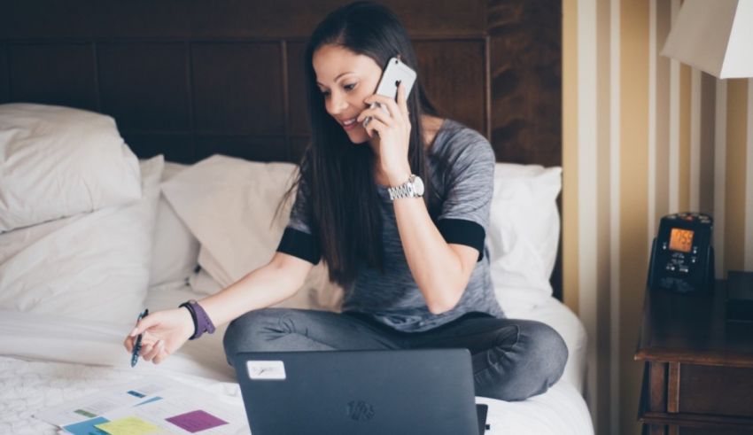 A woman sitting on a bed with a laptop and a cell phone.