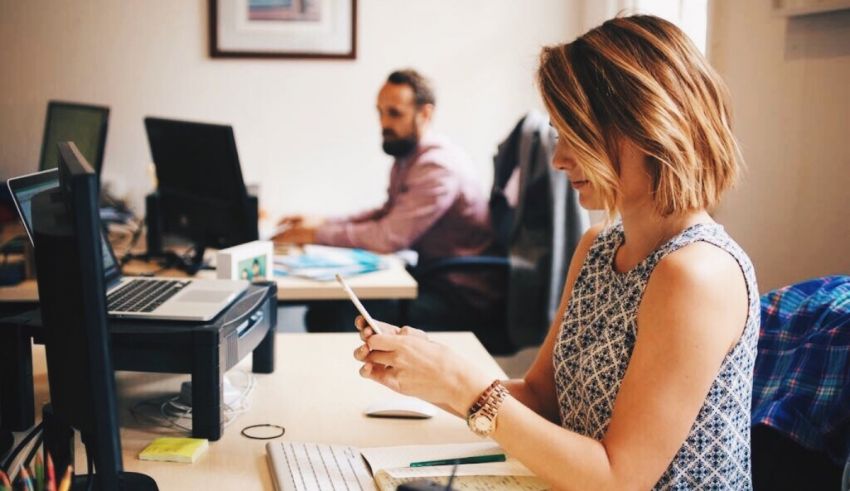 A woman sitting at a desk with a laptop and a cell phone.