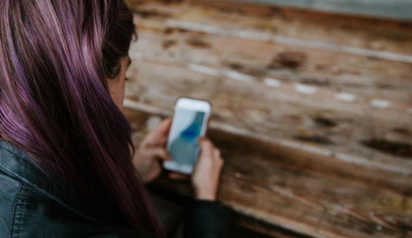 A woman with purple hair using her phone on a wooden table.