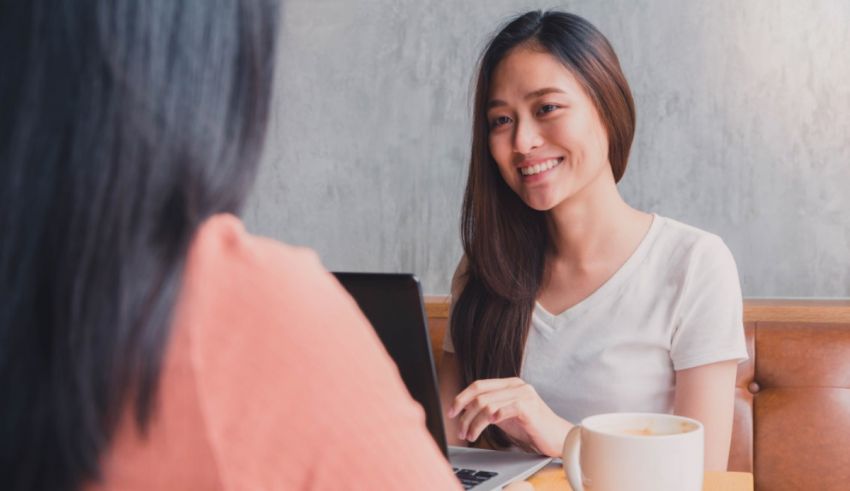 Two asian women sitting at a table and talking to each other.