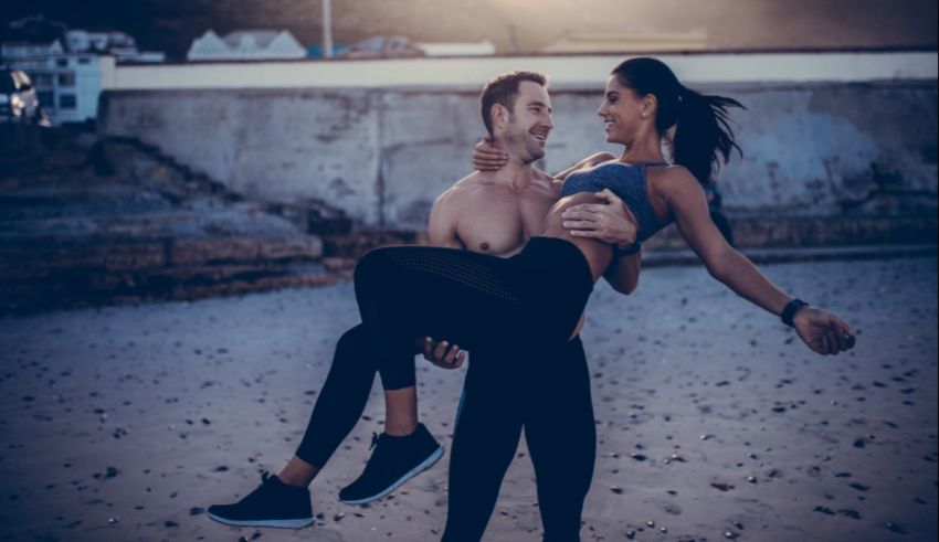 A man is carrying a woman on the beach.