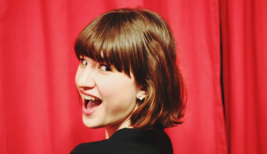 A young woman is smiling in front of a red curtain.