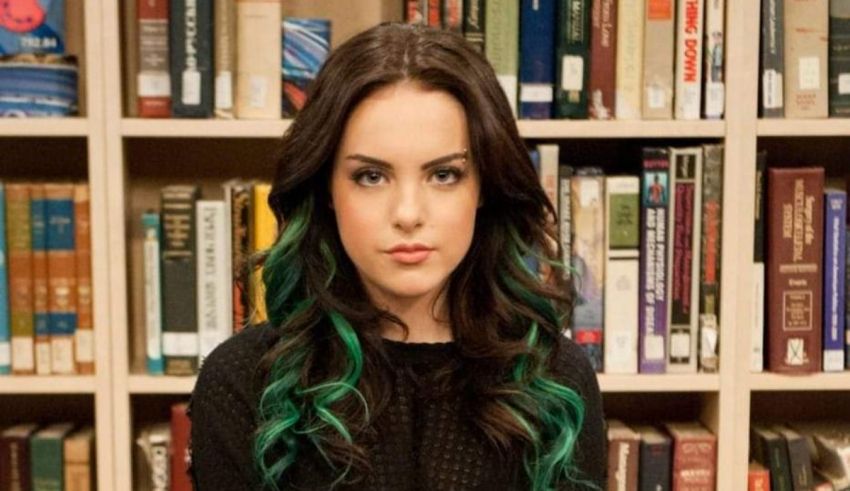 A woman with green hair in front of a bookshelf.