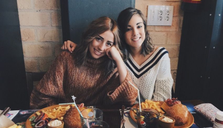 Two women sitting at a table with food and drinks.