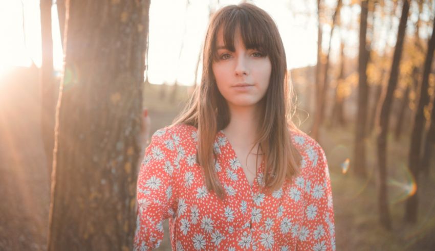 A woman in a floral shirt is standing in the woods.