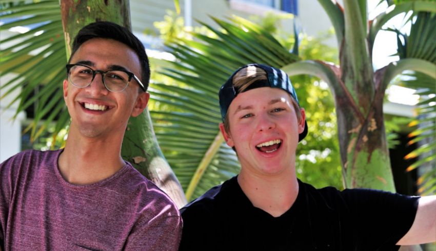 Two young men smiling in front of a palm tree.