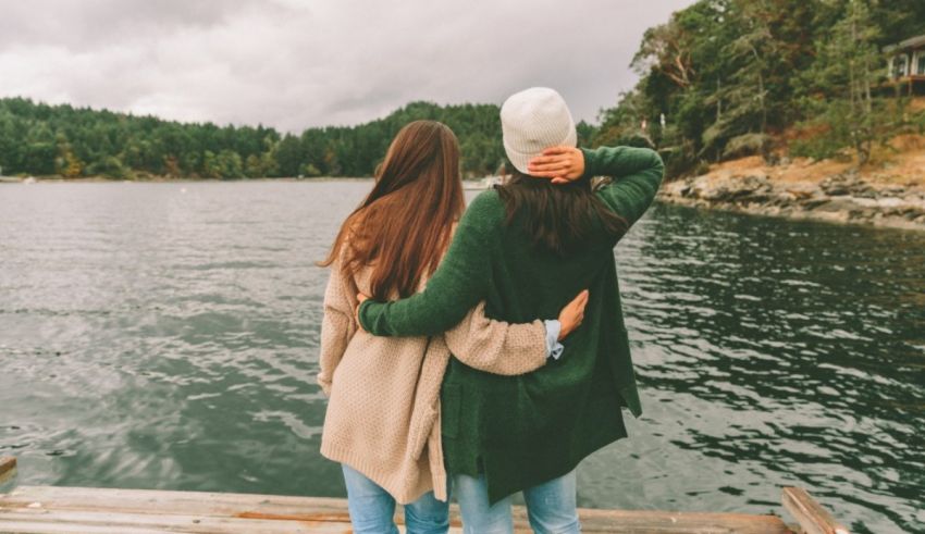 Two women standing on a dock next to a lake.