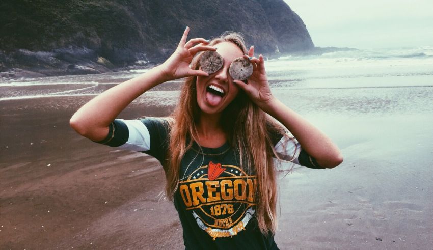 A girl holding up a pair of glasses on the beach.
