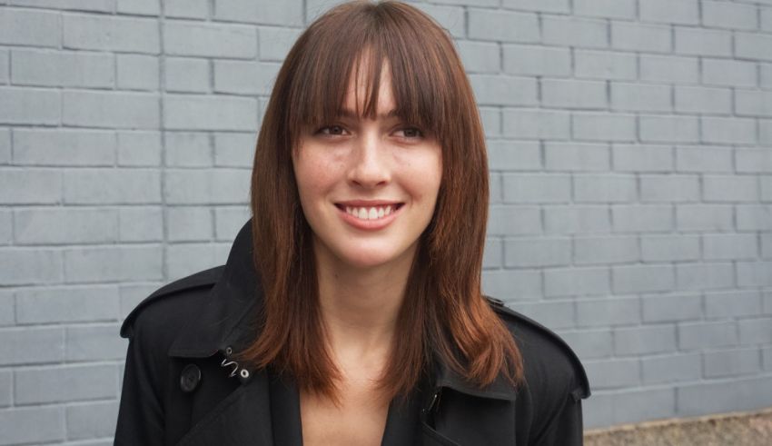 A woman in a black coat smiling in front of a brick wall.