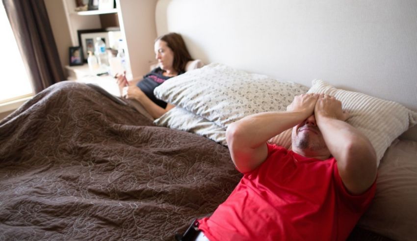 A man lying on a bed with his hands on his face.