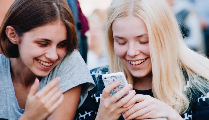 Two girls are smiling while looking at their cell phones.
