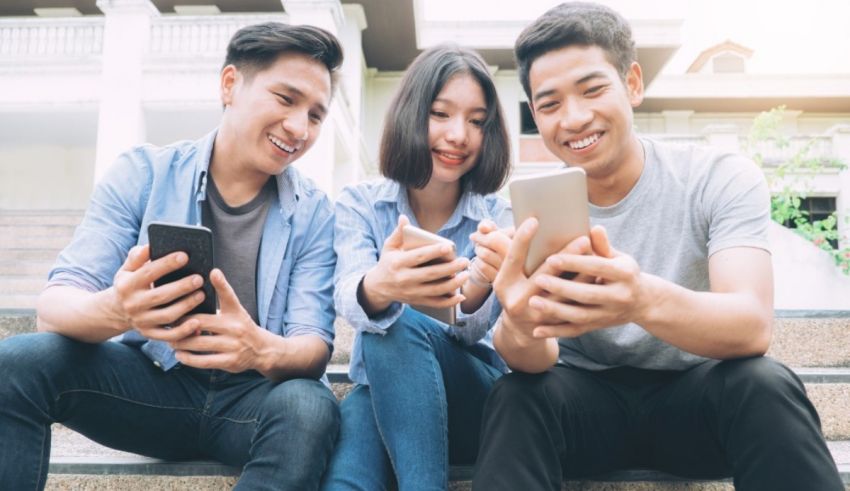 A group of young asian people sitting on steps and using cell phones.