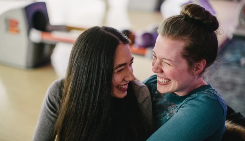 Two women laughing in a bowling alley.